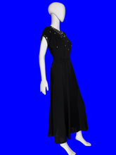 Load image into Gallery viewer, A black midi-length dress with short sleeves, a V-neckline, and delicate silver beaded embellishments around the neckline, displayed on a white mannequin.