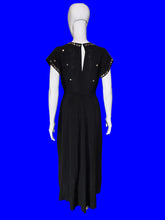 Load image into Gallery viewer, A black floor-length dress displayed on a white mannequin indoors. The dress has short sleeves with lace trim, a split neckline, and small metallic embellishments on the bodice and sleeves.