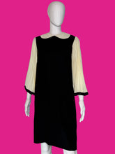 Load image into Gallery viewer, A black dress displayed on a white mannequin, featuring cream pleated three-quarter sleeves with black trim.