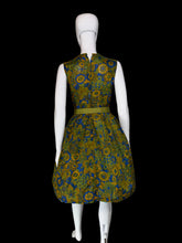 Load image into Gallery viewer, A sleeveless knee-length dress with a pleated skirt and matching belt, featuring a bold floral pattern in olive green, mustard yellow, and blue, displayed on a white mannequin.