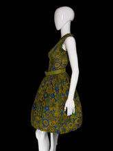 Load image into Gallery viewer, A sleeveless knee-length dress with a pleated skirt and matching belt, featuring a bold floral pattern in olive green, mustard yellow, and blue, displayed on a white mannequin.