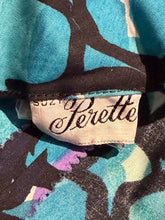 Load image into Gallery viewer, Close-up of a fabric label reading 'Perrette' sewn onto a patterned garment. The label is beige with black script, and the surrounding fabric has a bold abstract print in turquoise, black, cream, and small purple areas.
