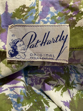 Load image into Gallery viewer, Close-up of a Pat Hartly fabric label sewn onto a vintage-style floral print garment. The label is cream-colored with blue embroidery.