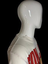 Load image into Gallery viewer, A close-up side view of a white mannequin torso wearing a cream-colored t-shirt with a bold red graphic print and a tear at the collar on the shoulder seam.
