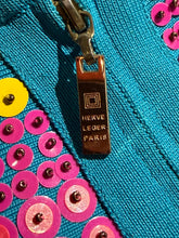 Load image into Gallery viewer, Close-up of a turquoise blue garment with a bronze-toned metal zipper pull engraved with 'HERVE LEGER PARIS'. The fabric is decorated with bright pink and yellow sequins.