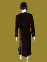 Load image into Gallery viewer, A dark brown velvet two-piece set consisting of a long-sleeve cropped jacket and matching midi length dress, displayed on a white mannequin from the back. The set includes a matching brown head covering.