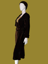 Load image into Gallery viewer, A dark brown velvet 1920s set featuring a midi length dress and matching long sleeve cropped jacket displayed on a white mannequin. The set includes a matching brown head covering.