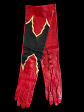 Load image into Gallery viewer, A pair of long red leather gloves laid flat on a textured gray surface, featuring a large black panel on one glove with yellow scalloped trim and three black buttons on the side.