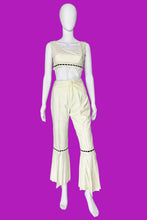 Load image into Gallery viewer, A cream-colored two-piece outfit displayed on a white mannequin. The set includes a sleeveless crop top with black dashed trim and matching high-waisted flared pants with black dashed trim and decorative buttons on the back.