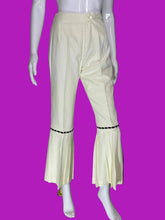 Load image into Gallery viewer, Cream-colored cropped flare pants with pleated flared hems and black embroidered trim, displayed on a white mannequin.
