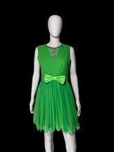 Load image into Gallery viewer, A bright green sleeveless dress displayed on a white mannequin. The dress has a lace V-neck bodice, a matching green bow at the waist, and a pleated tulle skirt.
