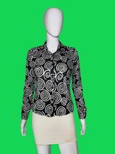 Load image into Gallery viewer, A long-sleeve button-up blouse with a black and white spiral swirl pattern, displayed on a white mannequin torso.