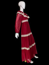 Load image into Gallery viewer, A long maroon chiffon and lace prairie dress displayed on a white mannequin from the side, featuring sheer long sleeves, a square neckline with cream lace trim, and matching lace bands at the waist and hem.