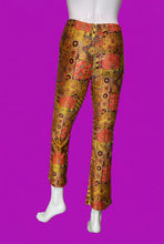 Load image into Gallery viewer, A pair of cropped pants displayed on a white mannequin. The pants feature a vibrant, multicolored patchwork print with orange, red, yellow, and black geometric and floral motifs.