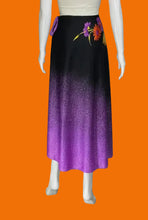 Load image into Gallery viewer, A long A-line skirt displayed on a white mannequin. The skirt features a black-to-purple ombré gradient with a floral print near the waistband in purple, orange, and yellow.