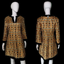 Load image into Gallery viewer, A women's tunic dress shown on a white mannequin from both front and back views. The dress features a bold geometric chain-link pattern in orange, black, and beige, with solid black trim at the split neckline, cuffs, and hem.
