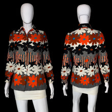 Load image into Gallery viewer, A long-sleeve button-front blouse shown on a white mannequin from front and back views. The shirt features a bold retro floral pattern with large orange, black, and cream flowers, plus vertical striped details and a dark gray ribbed hem.
