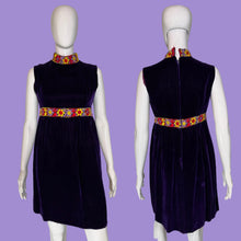 Load image into Gallery viewer, A sleeveless deep purple velvet dress displayed on a white mannequin, showing both front and back views. The dress features a high mock neck, a colorful patterned waistband with yellow, red, and blue floral motifs, and a matching patterned collar.
