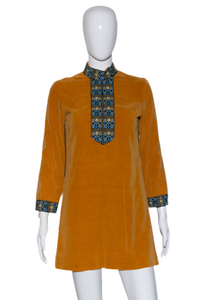 Mustard yellow dress with patterned details on a mannequin against a white background
