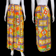 Load image into Gallery viewer, A long printed skirt on a white mannequin from the front and back. The skirt has a bold geometric and floral pattern in yellow, orange, purple, green, and cream, with an elastic waistband.
