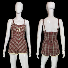 Load image into Gallery viewer, A plaid bathingsuit displayed on white mannequins, showing both front and back views. The romper features a brown, red, green, and beige plaid pattern with cream-colored trim and a matching cream drawstring on the front.
