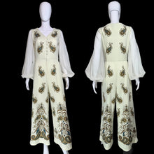 Load image into Gallery viewer, A cream-colored jumpsuit with sheer long sleeves and ornate paisley embroidery in gold, brown, and teal, displayed on a mannequin from both front and back views.
