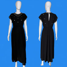 Load image into Gallery viewer, A black midi dress with gold embellishments, shown from both the front and back on a white mannequin. The dress features short cap sleeves, a round neckline decorated with gold studs and beads, and a back keyhole cutout with gold buttons.
