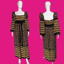 Load image into Gallery viewer, A vintage maxi dress displayed on a white mannequin showing the front and side details. The dress features a black base with yellow stripes on the sleeves and hem, and a pink floral pattern on the bodice and skirt.

