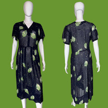 Load image into Gallery viewer, A short-sleeve midi dress displayed on a white mannequin, shown from both the front and back views. The dress is navy blue with a green leaf print and small green, teal, and cream speckled details.

