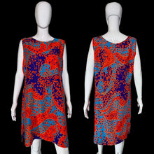 Load image into Gallery viewer, A sleeveless A-line dress displayed on a white mannequin, showing both front and back views. The dress features a vibrant paisley pattern in red, orange, and blue on a dark navy background.

