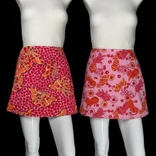Load image into Gallery viewer, Two pink patterned mini skirts displayed on white mannequin. The left skirt has a red and orange polka-dot base with large orange butterfly motifs.
