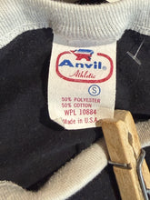 Load image into Gallery viewer, Anvil athletic tag on a black garment with a wooden clothespin.
