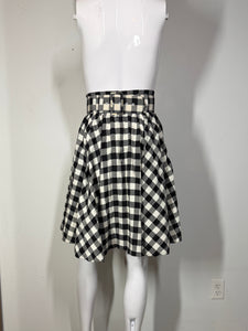 Mannequin wearing a black and white checkered skirt against a plain wall.