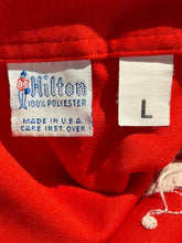 Load image into Gallery viewer, Close-up of a red garment with a label on a red background
