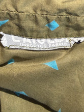 Load image into Gallery viewer, Close-up of a label on a green fabric with blue patterns
