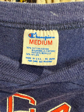 Load image into Gallery viewer, Close-up of a Champion label on a blue garment with orange lettering.
