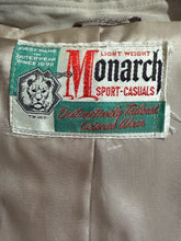 Load image into Gallery viewer, Close-up of a garment interior label reading 'Monarch Sport-Casuals' with a lion emblem and green and red text on a light beige fabric background.
