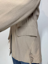 Load image into Gallery viewer, Close-up of a beige jacket with a side pocket, worn over blue jeans against a plain white background.
