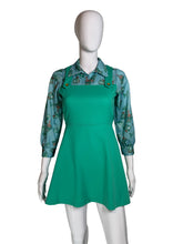Load image into Gallery viewer, A vintage green pinafore dress displayed on a white mannequin. The dress features a solid green body with a printed collar and shoulder straps, accented by three decorative buttons.
