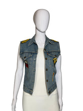 Load image into Gallery viewer, A light blue denim vest displayed on a white mannequin. The vest has yellow patches on the shoulders, a yellow circular patch on the chest, and a small red-and-white rectangular patch near the lower right side.
