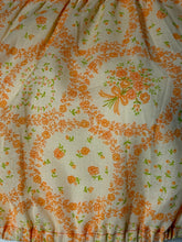 Load image into Gallery viewer, A close-up of a fabric surface with a repeating orange floral border and bow pattern on a warm off-white background.
