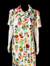 Load image into Gallery viewer, A white short-sleeve button-up dress with a vibrant multicolor floral print, displayed on a white mannequin torso.
