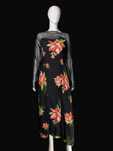 Load image into Gallery viewer, A black midi dress with a vibrant pink and red floral print and sheer black long sleeves, displayed on a white mannequin in front of a black background.
