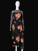 Load image into Gallery viewer, A black maxi dress with a vibrant red and pink floral print and sheer black mesh sleeves, displayed on a white mannequin in front of a black background.
