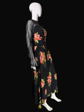 Load image into Gallery viewer, A black dress with a vibrant red, pink, and green floral print, displayed on a white mannequin. The dress features sheer black mesh long sleeves, set against a black background.
