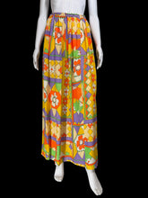 Load image into Gallery viewer, A mannequin wearing a long skirt with a bold geometric and floral pattern in yellow, orange, purple, green, and cream.
