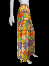 Load image into Gallery viewer, A mannequin wearing a long skirt with a bold geometric and floral pattern in yellow, orange, purple, green, and cream.
