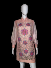 Load image into Gallery viewer, A pink embroidered tunic dress shown on a white mannequin. The dress features long sheer sleeves, a mandarin collar, and intricate floral and scroll embroidery in pink, purple, and gold.
