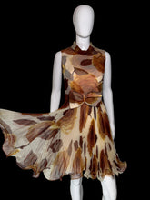 Load image into Gallery viewer, A sleeveless fit-and-flare dress displayed on a white mannequin. The dress features a brown and beige abstract leaf print on a sheer mesh fabric, with a matching waist sash and bow detail on the front. 

