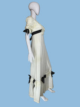 Load image into Gallery viewer, A vintage-style cream maxi dress displayed on a white mannequin from both front and back views, featuring black ribbon bows, lace trim, and a long black sash at the back.
